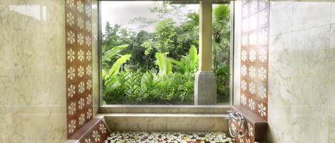 A bathroom with a large window, a marble floor, and a small sink area with a flower arrangement.