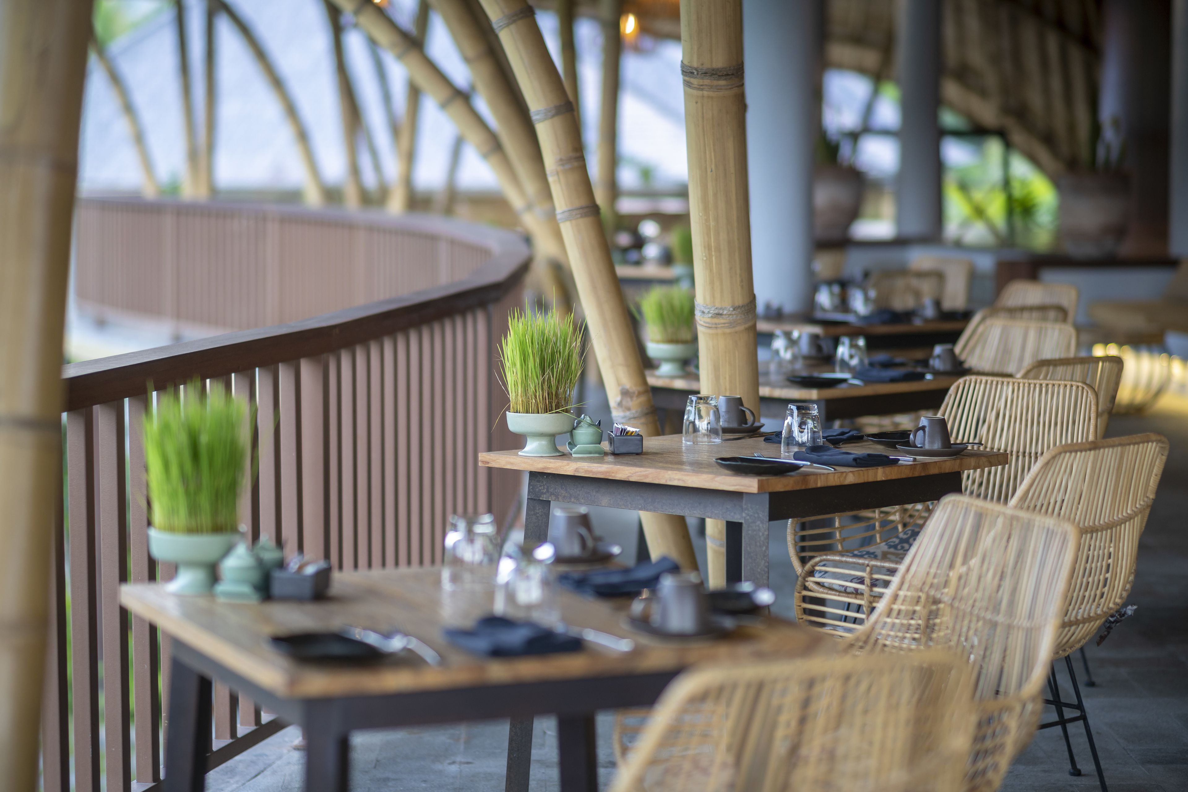 An outdoor dining area with bamboo columns, wicker chairs, and tables set for dining.