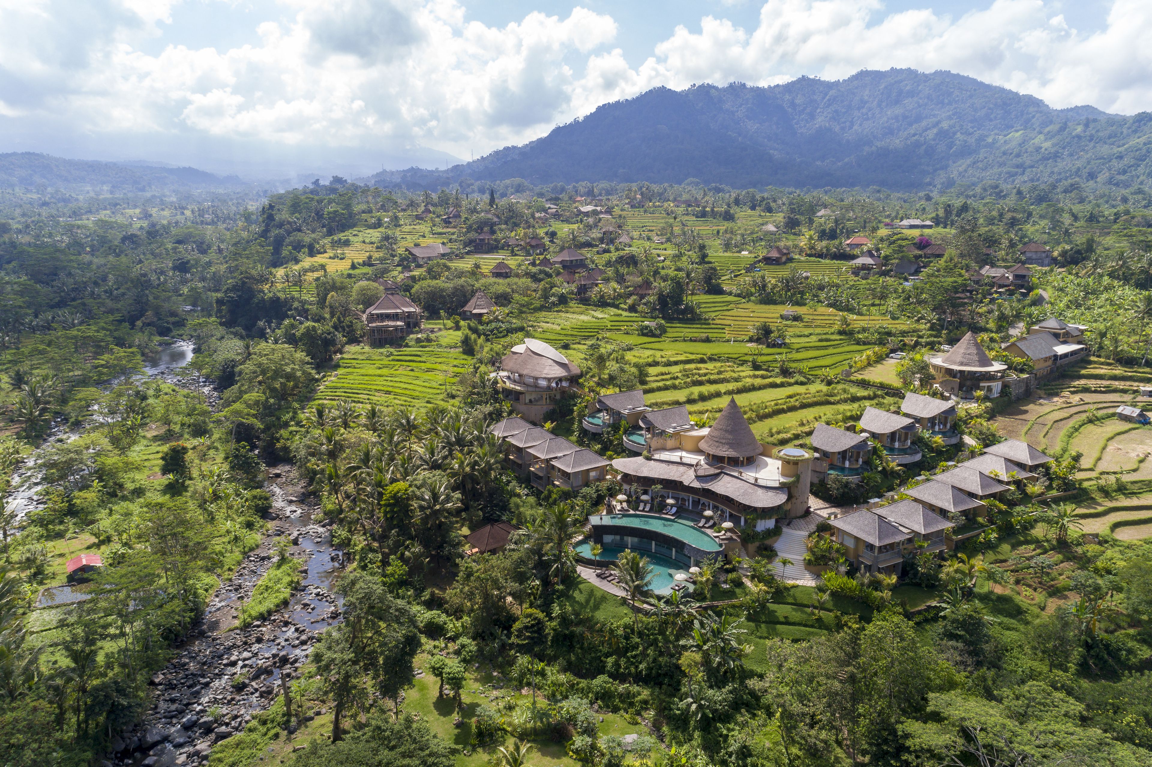 A resort with multiple buildings, a swimming pool, and terraced fields in the background.