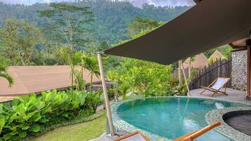 A pool area with wooden deck, lounge chairs, and a view of a lush forested hillside.