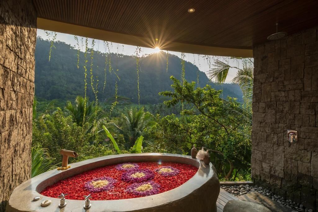 A spa area with a hot tub surrounded by red and purple flowers, set against a backdrop of lush greenery and mountains.