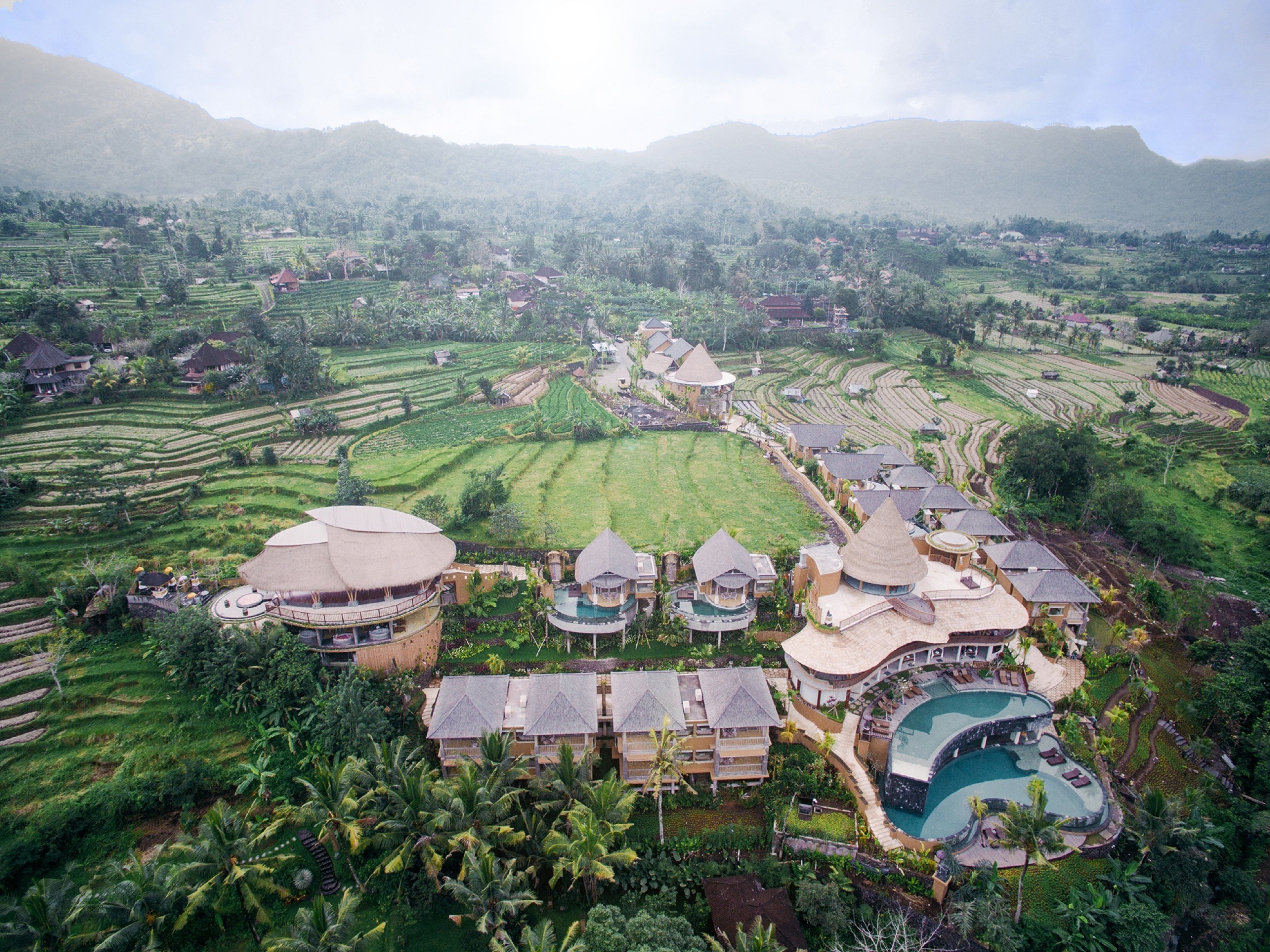 A resort with multiple bungalow-style buildings, a large central pool, and terraced rice fields in the background.