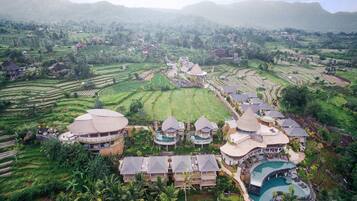 A resort with multiple bungalow-style buildings, a large central pool, and terraced rice fields in the background.