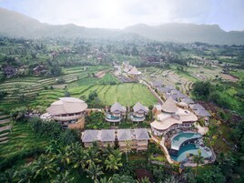 Un resort con varias edificaciones tipo bungalow, una amplia piscina central y terrazas de arrozales al fondo.