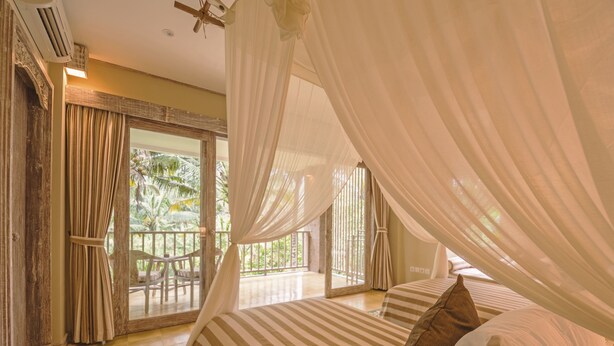 Un dormitorio con una cama grande, ropa de cama a rayas y un dosel. Cuenta con un balcón con vistas a palmeras.