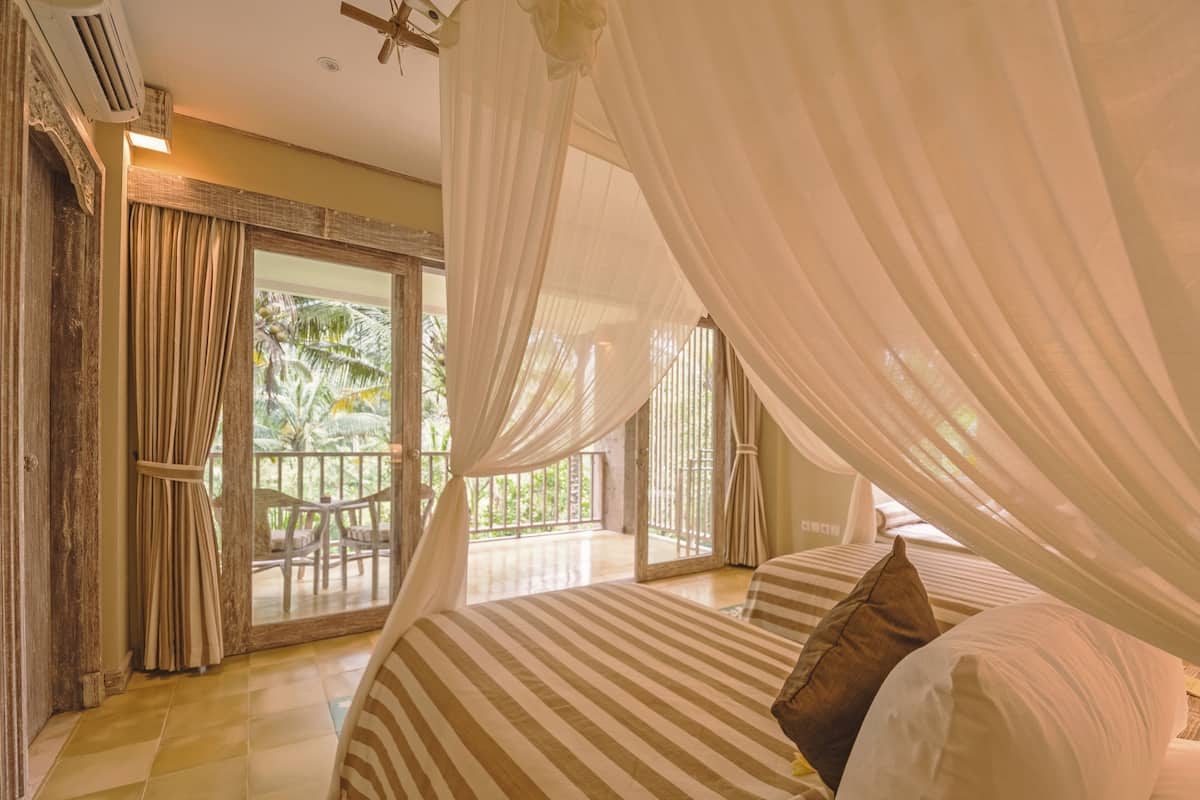 Un dormitorio con una cama grande, ropa de cama a rayas y un dosel. Cuenta con un balcón con vistas a palmeras.