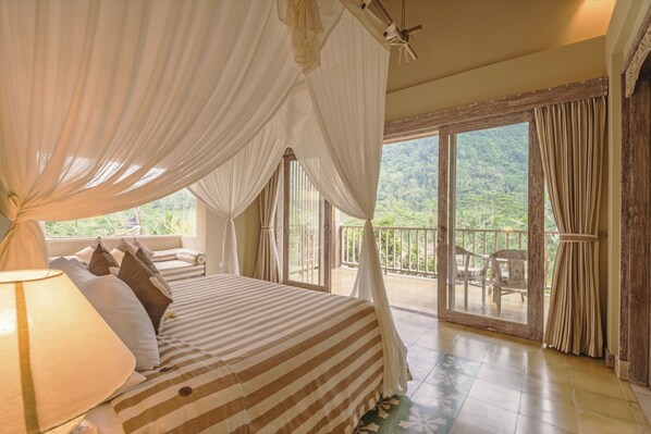 A bedroom with a large bed, a canopy, and a balcony with a view of greenery.