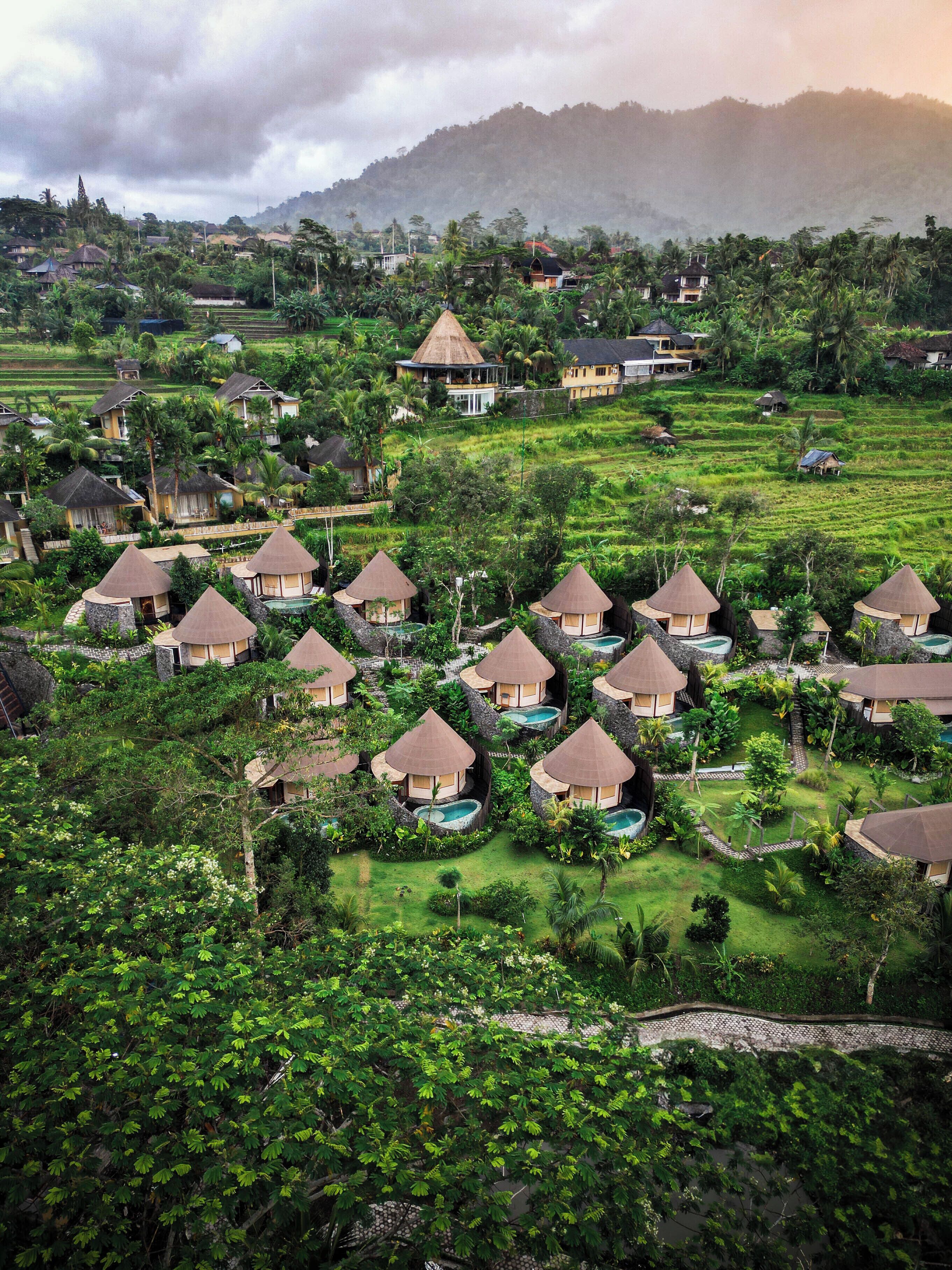 Een resort met bungalows met rieten daken, privézwembaden en weelderige groene begroeiing.
