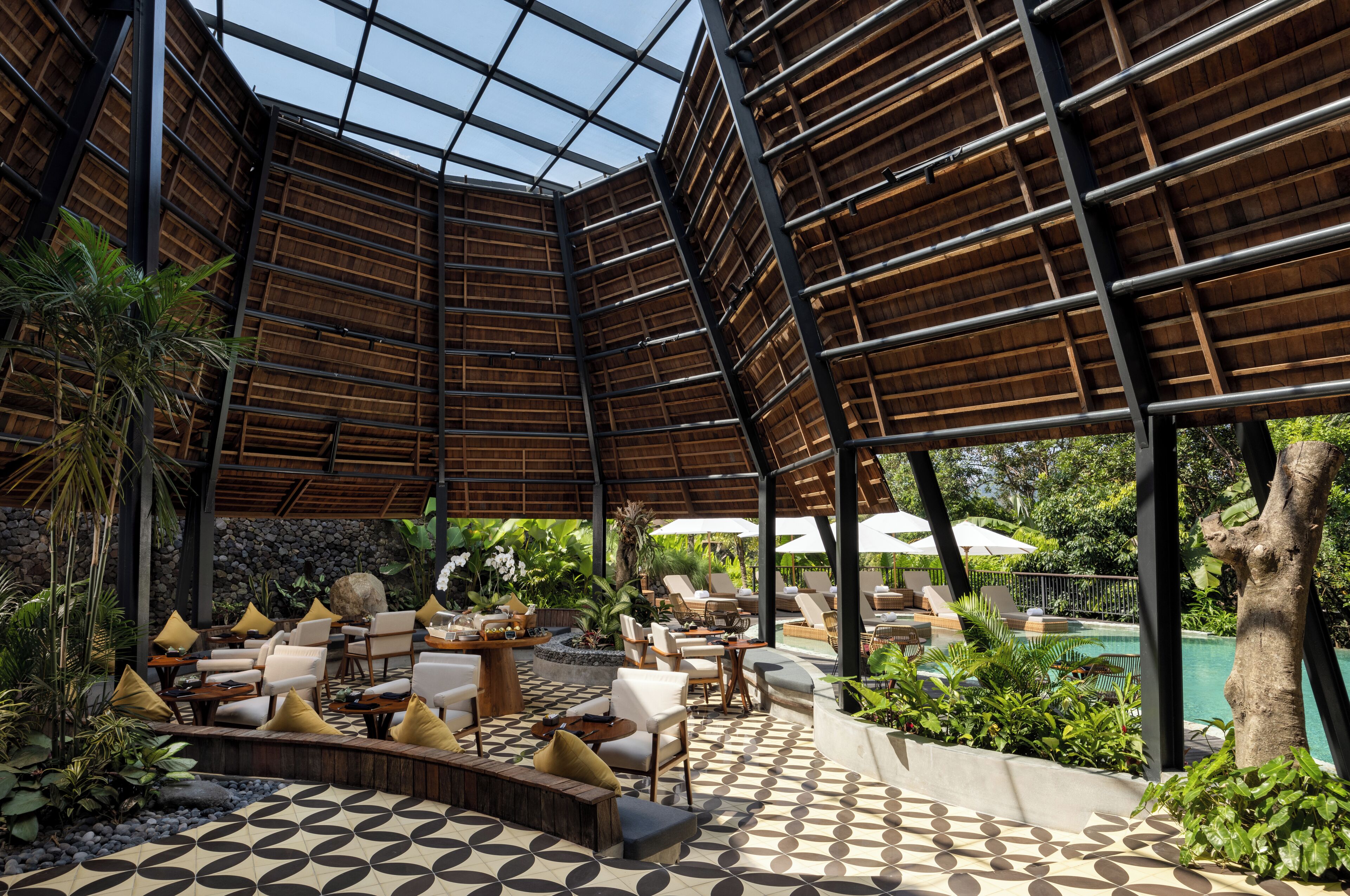 An outdoor lounge area with a geometric patterned floor, wooden pergola, and seating arrangements.