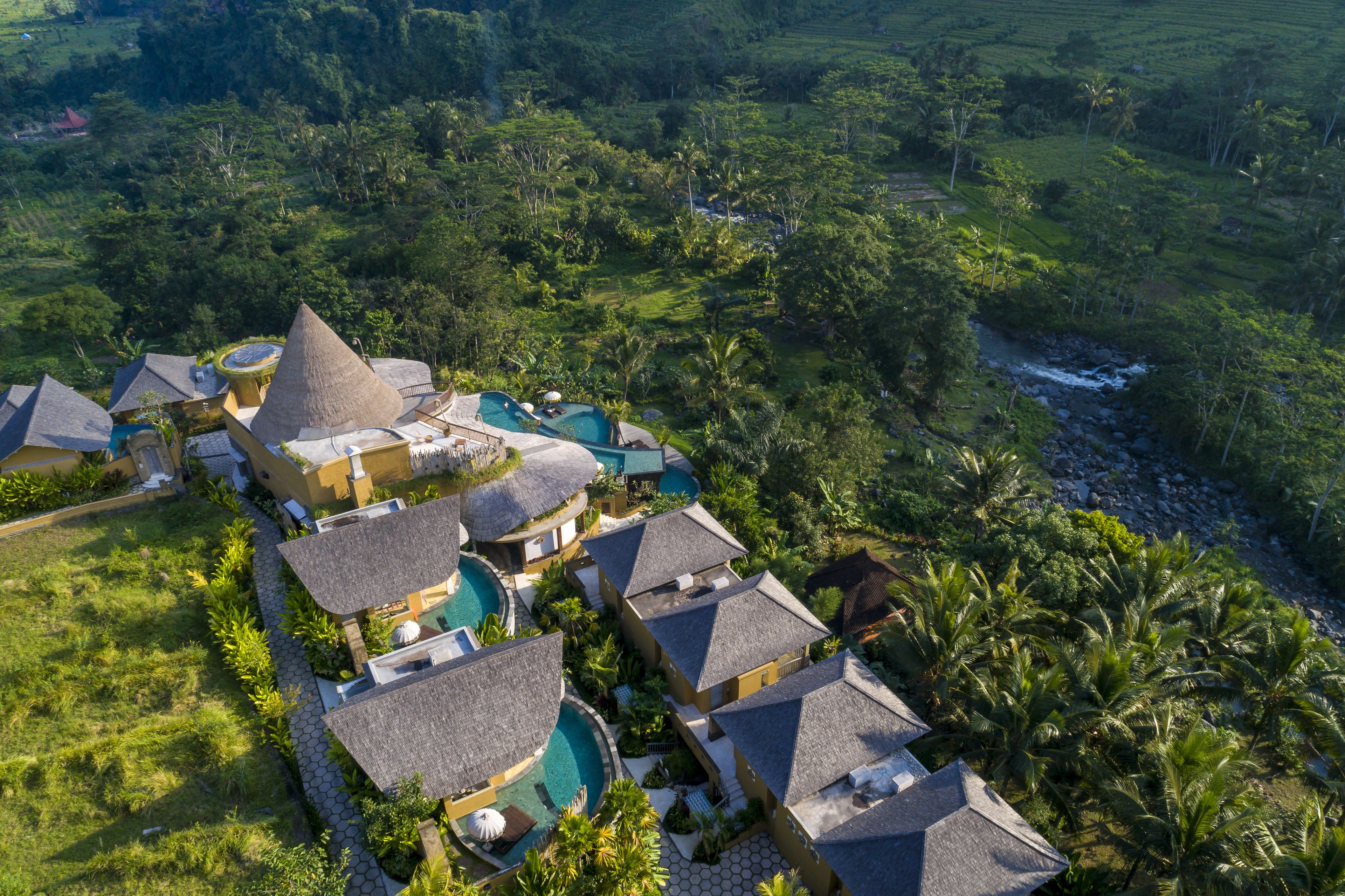 A resort with multiple bungalow-style buildings, a central swimming pool, and lush surrounding vegetation.
