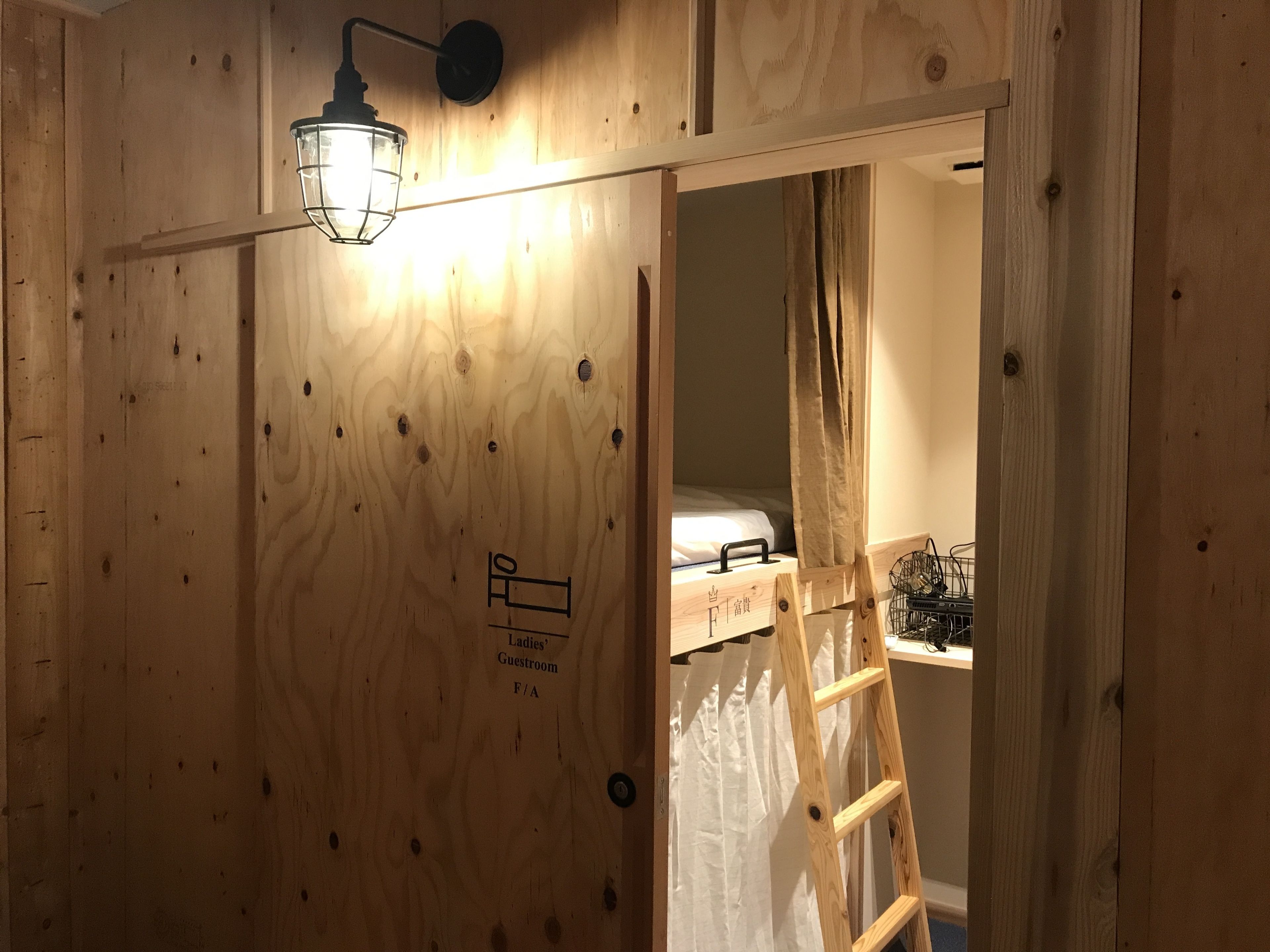 A wooden room with a ladder, a bed, and a light fixture.