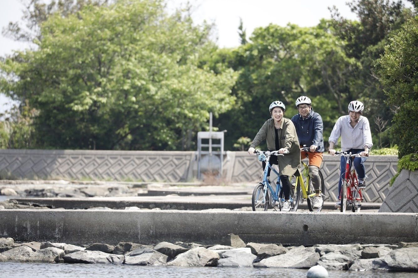 Three cyclists on a bridge with a stone wall and greenery in the background.