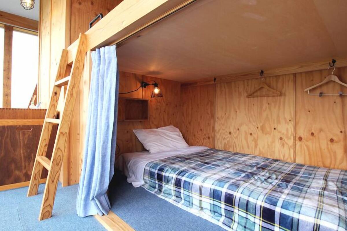 A wooden cabin room with a bunk bed, a ladder, a hanging light fixture, and a wooden wardrobe.