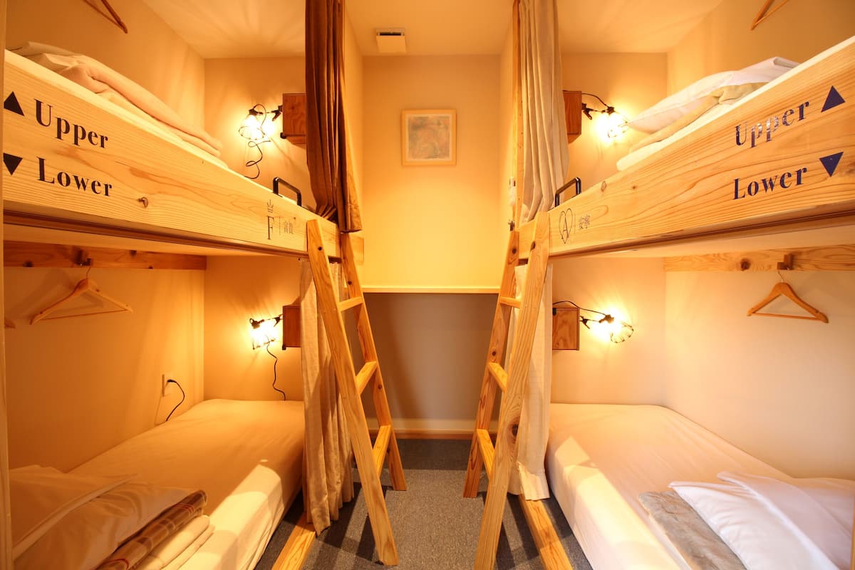 A room with two bunk beds labeled "Upper Lower," each with a wooden ladder and a wall-mounted light.