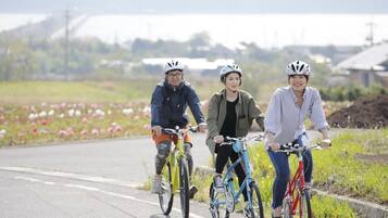 Three people riding bicycles on a paved path with flowers on the side.