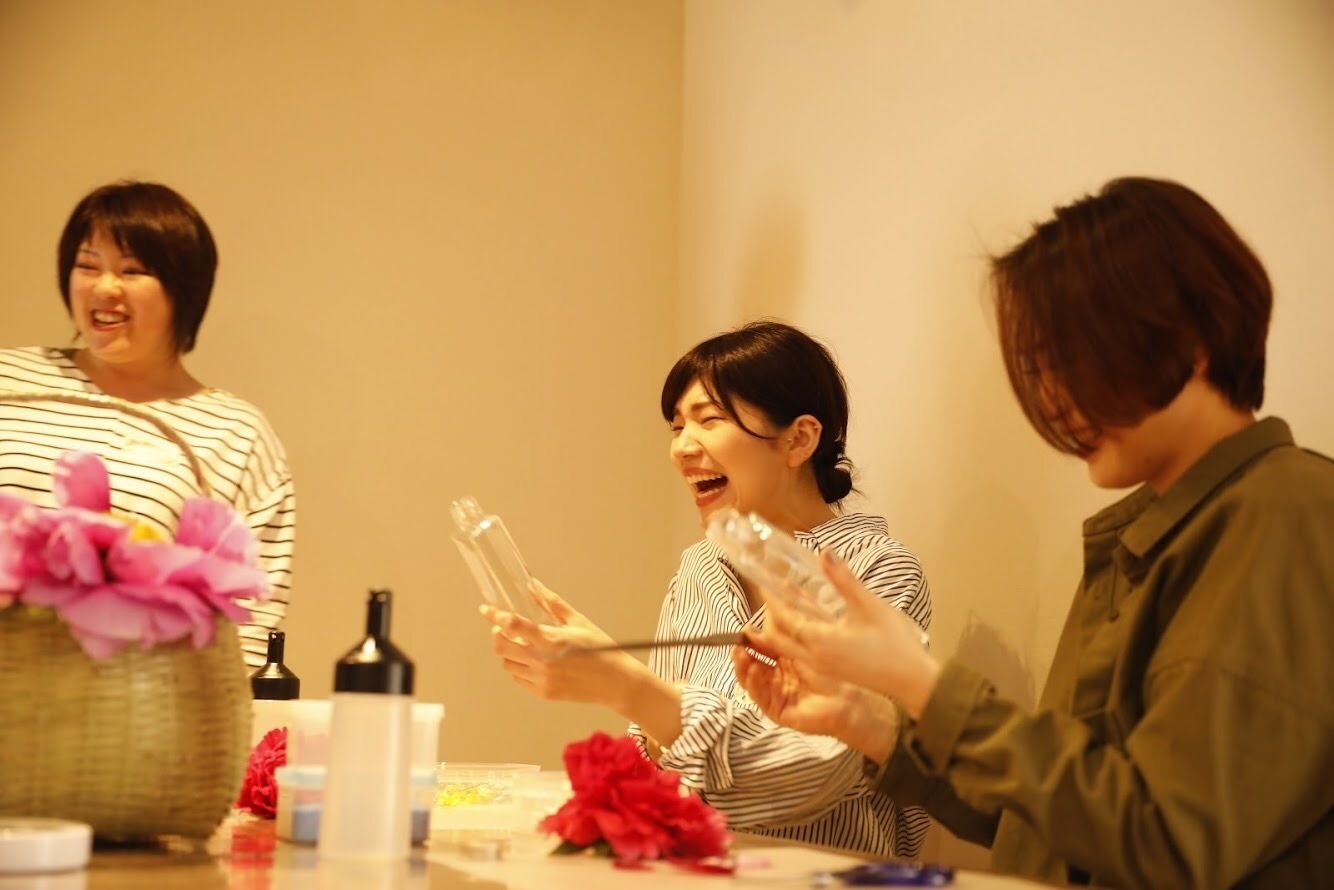 A group of people sitting around a table with various items, including bottles and a basket with flowers.