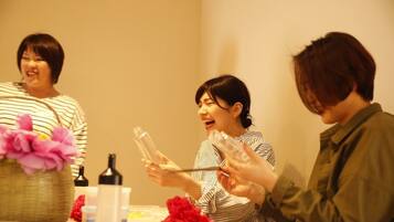 A group of people sitting around a table with various items, including bottles and a basket with flowers.