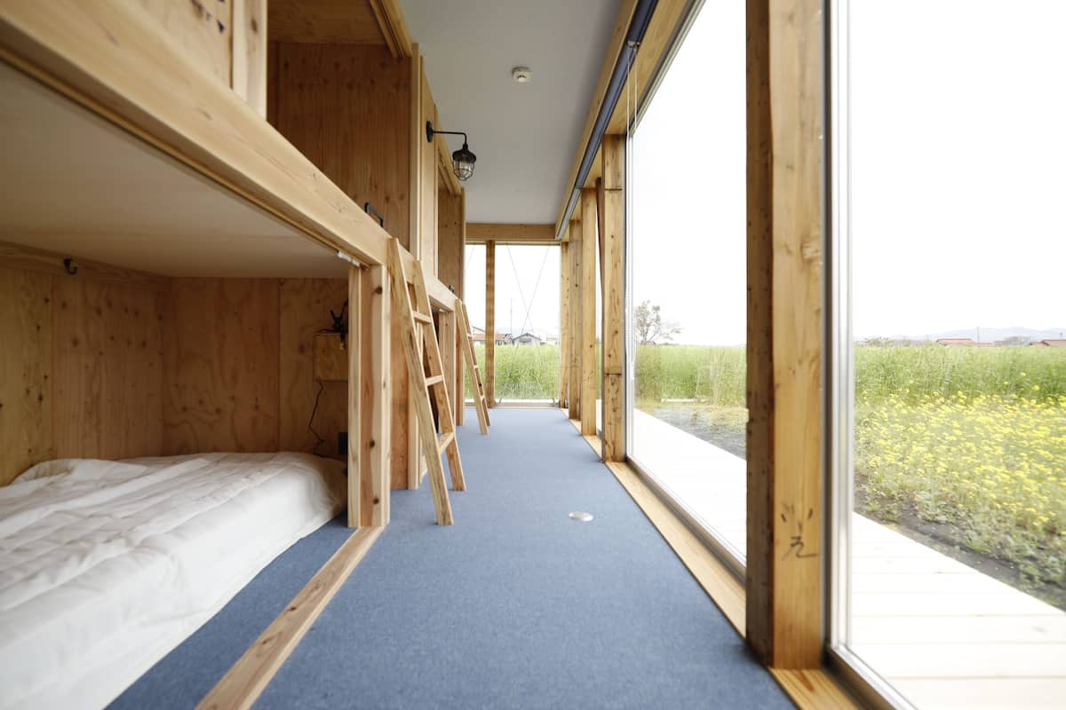 A room with a bunk bed, a ladder, and a window with a view of a field.