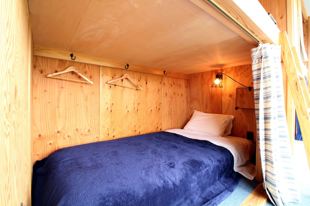 A small, cozy room with a single bed, wooden walls, and a hanging light fixture.