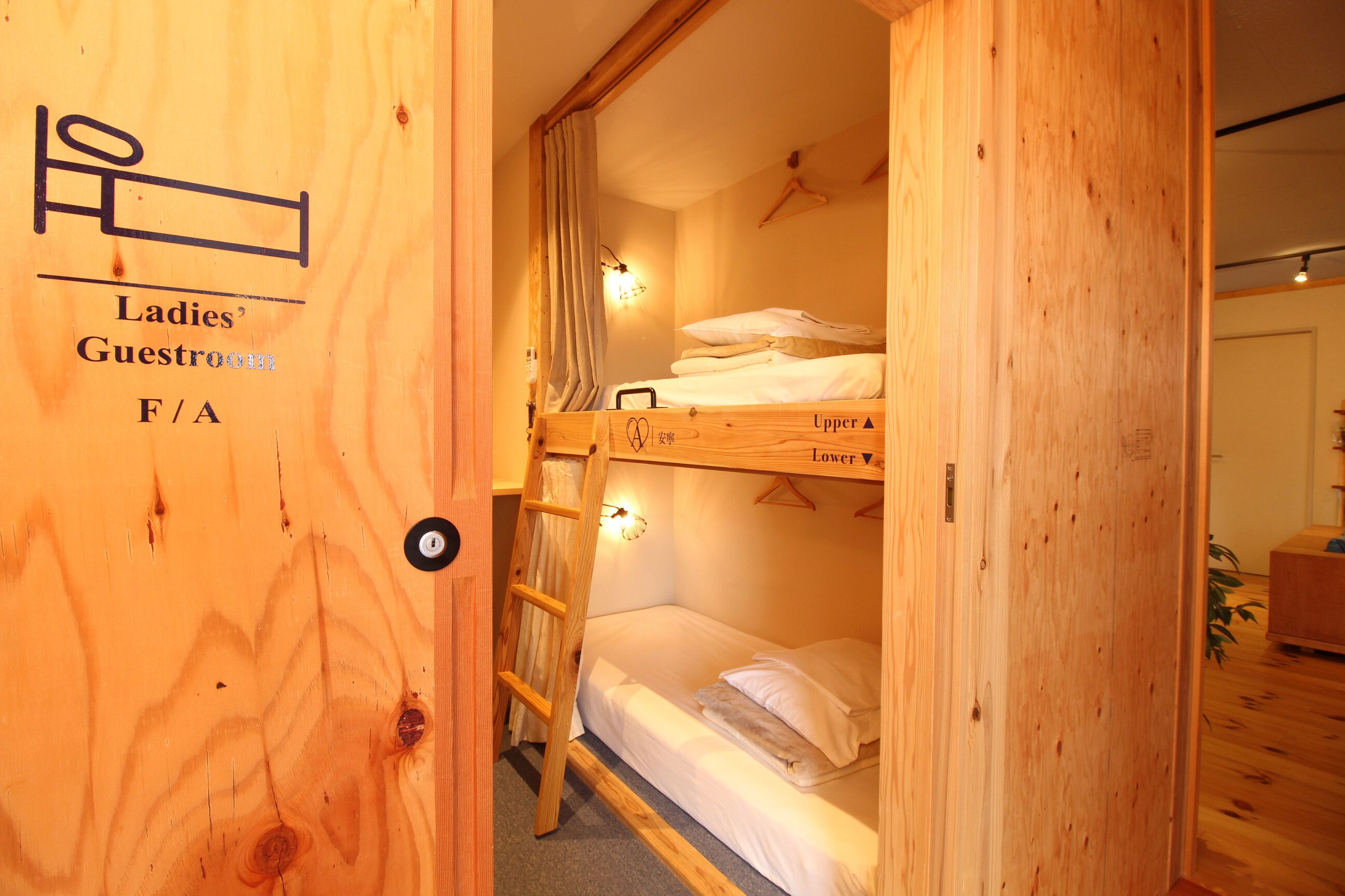 A wooden bunk bed room with a ladder, a hanging light fixture, and a door labeled "Ladies' Guestroom F/A".