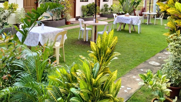 A courtyard with outdoor seating, potted plants, and a building with a tiled roof. - Mingche Apartment (Panglao)