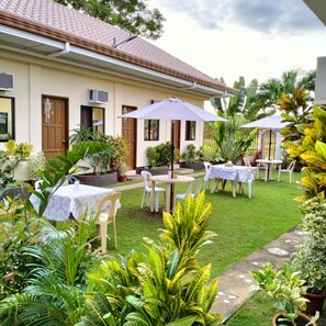 A courtyard with outdoor seating, potted plants, and a building with a tiled roof. - Mingche Apartment (Panglao)