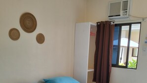 A single bed with blue bedding, a brown curtain, and a wall-mounted air conditioner. - Mingche Apartment (Panglao)