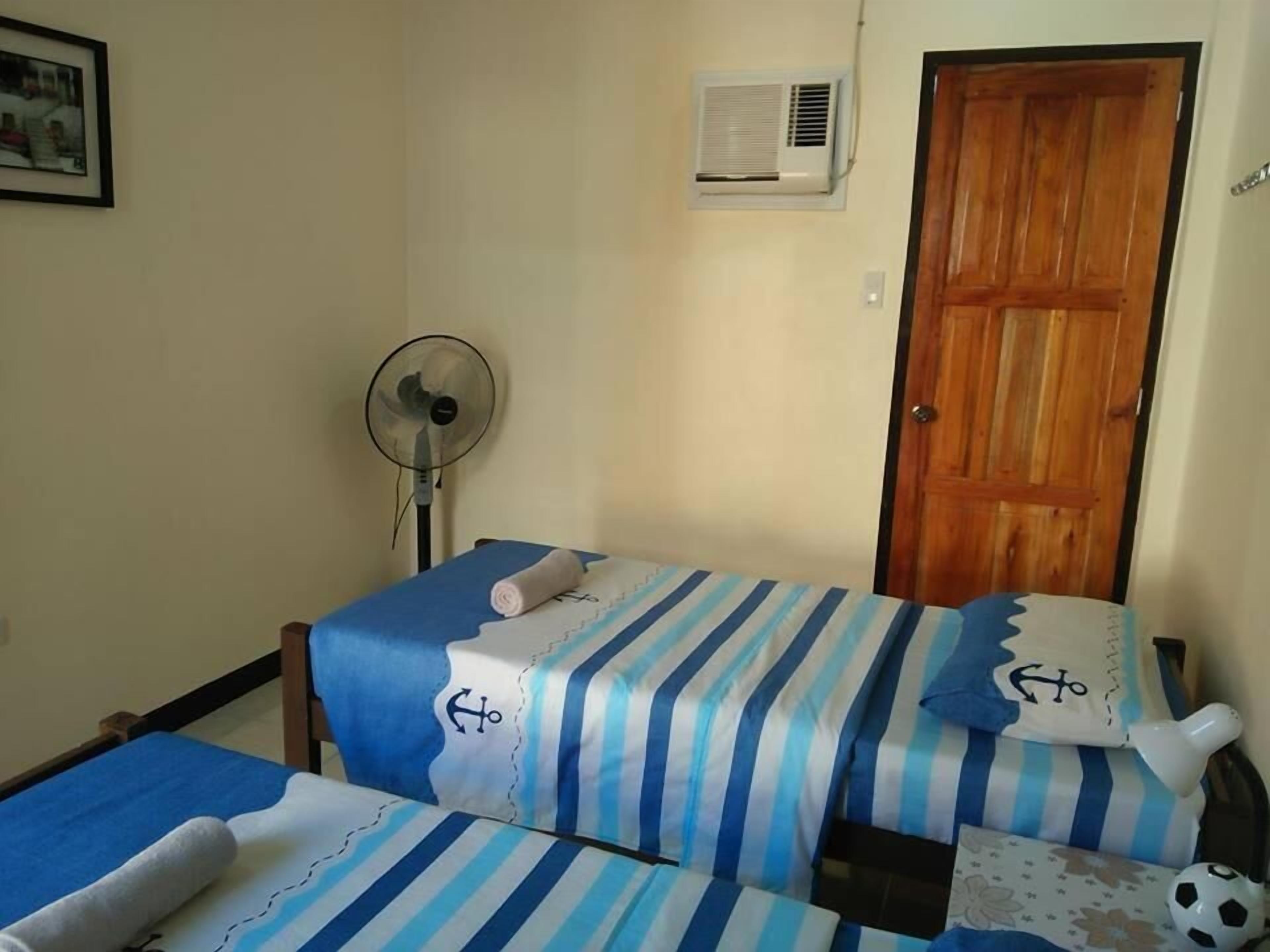 Una habitación con dos camas, un ventilador, una puerta de madera y un equipo de aire acondicionado.