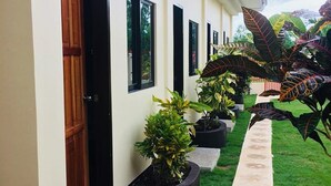A building with a series of doors and windows, a grassy area with potted plants, and a concrete pathway. - Mingche Apartment (Panglao)