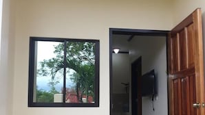 A room with a wooden door, a small table, two plastic chairs, and a framed picture on the wall. - Mingche Apartment (Panglao)