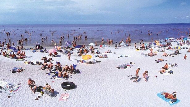 Una spiaggia affollata con persone che prendono il sole e nuotano.