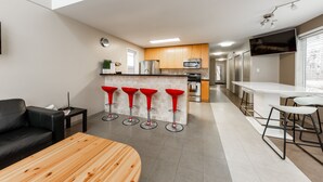 Una cucina moderna con isola centrale, sgabelli rossi, un divano in pelle nera e un tavolo in legno.