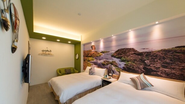 Habitación de hotel con dos camas, una pared de acento verde, un mural de un paisaje rocoso y un televisor de pantalla plana montado en la pared.