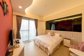 A modern hotel room with a large bed, a desk with a computer, and a vanity with toiletries.