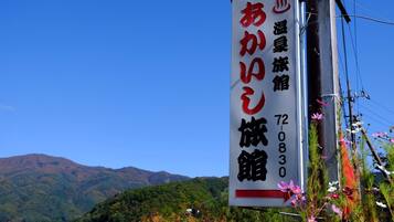 A sign for a hotel with Japanese characters, a mountain backdrop, and some flowers.