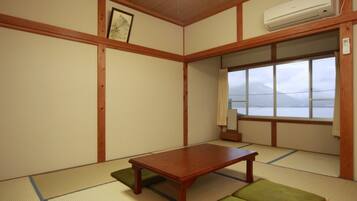 A traditional Japanese room with tatami flooring, a wooden table, and a window with a view of mountains.