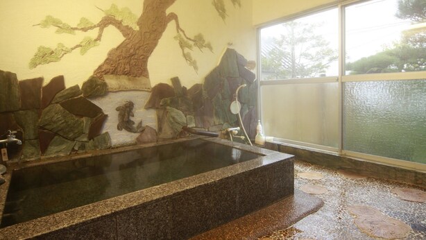 Una bañera de piedra con un mural de piedra, una ventana con vistas a árboles y un suelo de piedra.
