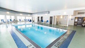 Una piscina interior con suelo de baldosas, sillas de descanso y zona de vestuarios.