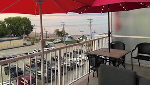 Un balcón con sombrillas rojas, vista al mar y un estacionamiento con coches.