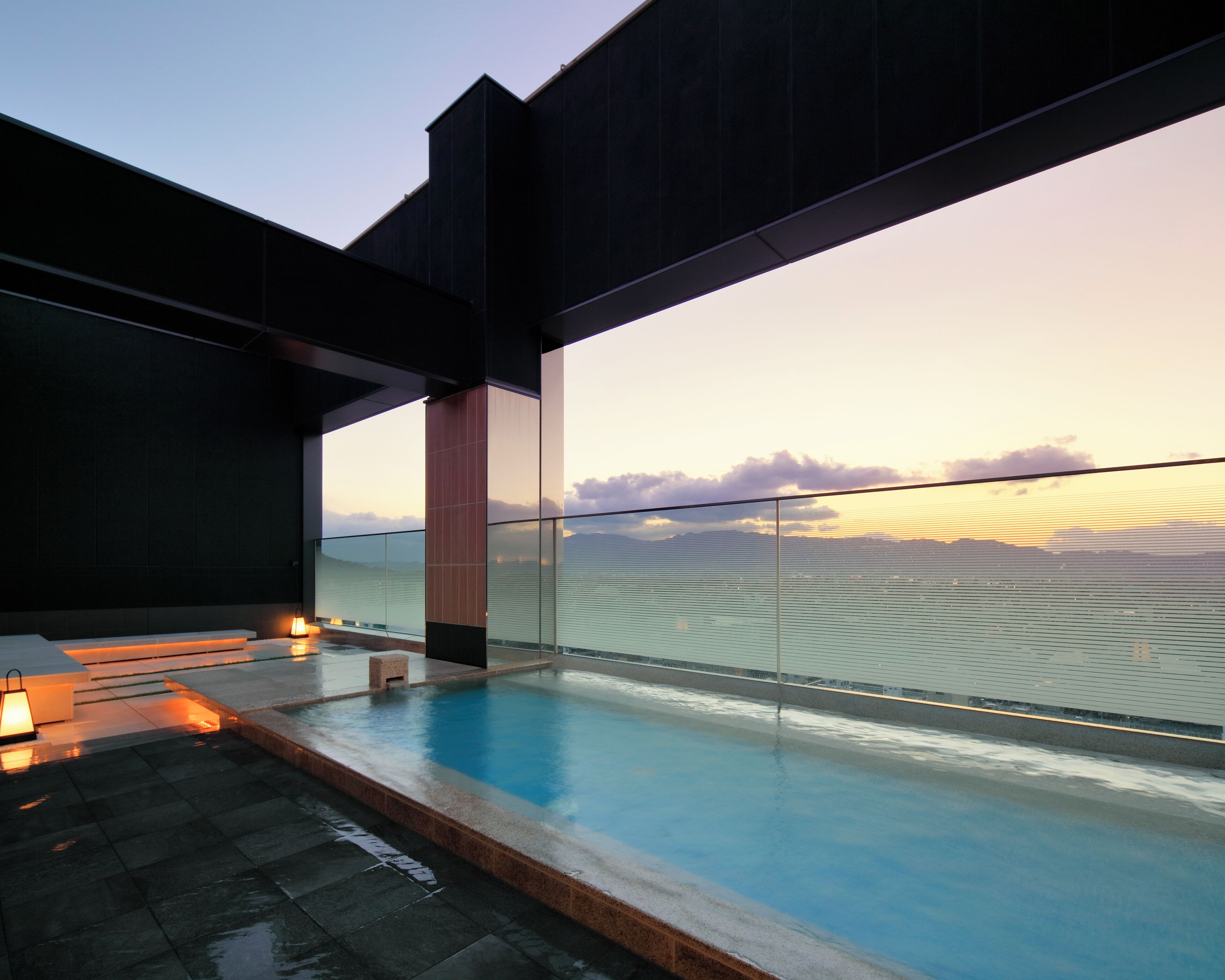 A modern infinity pool with a glass barrier, a sunset view, and a minimalist architectural design.
