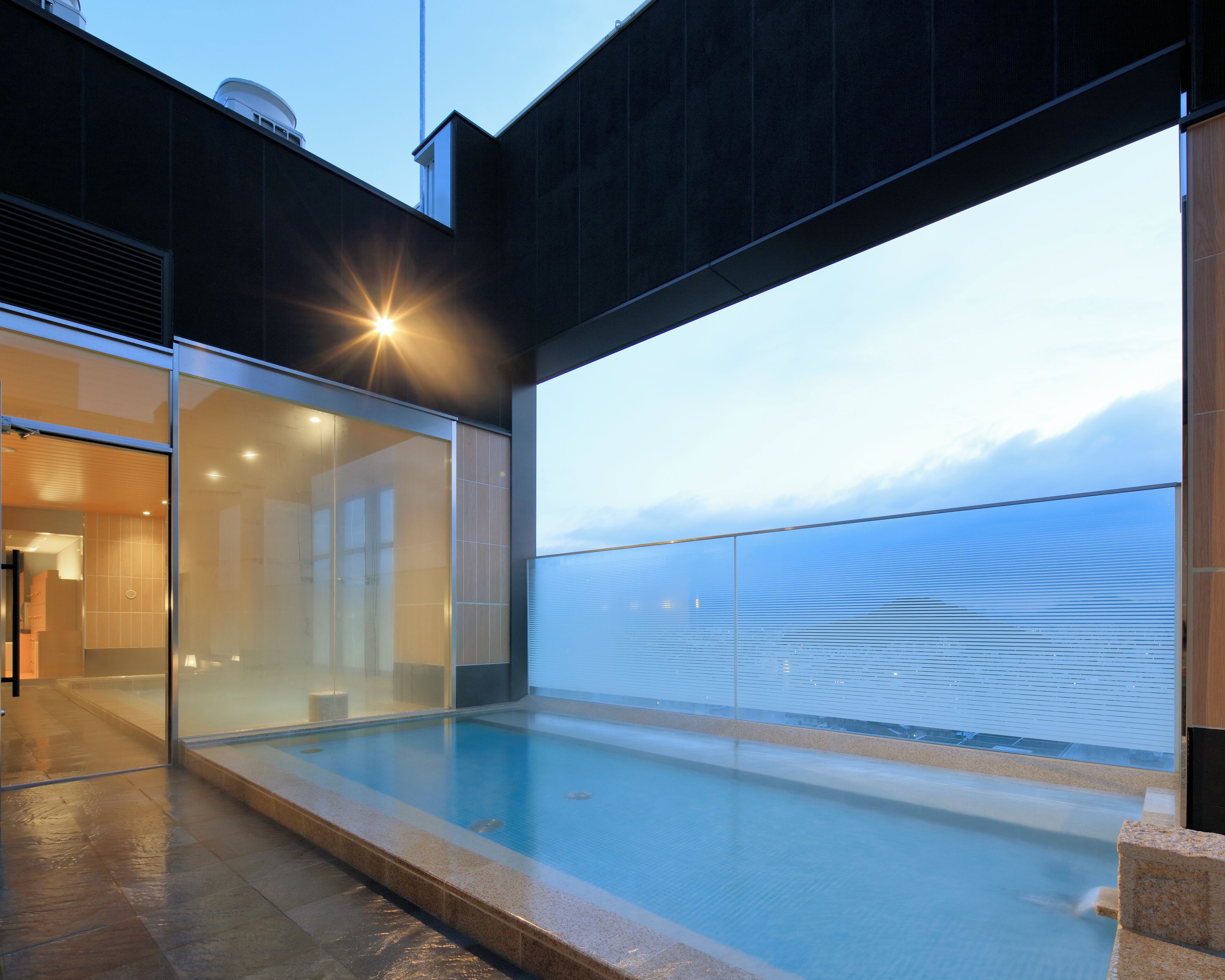 A modern building with a glass-enclosed infinity pool, a clear view of the sky, and a minimalist architectural design.