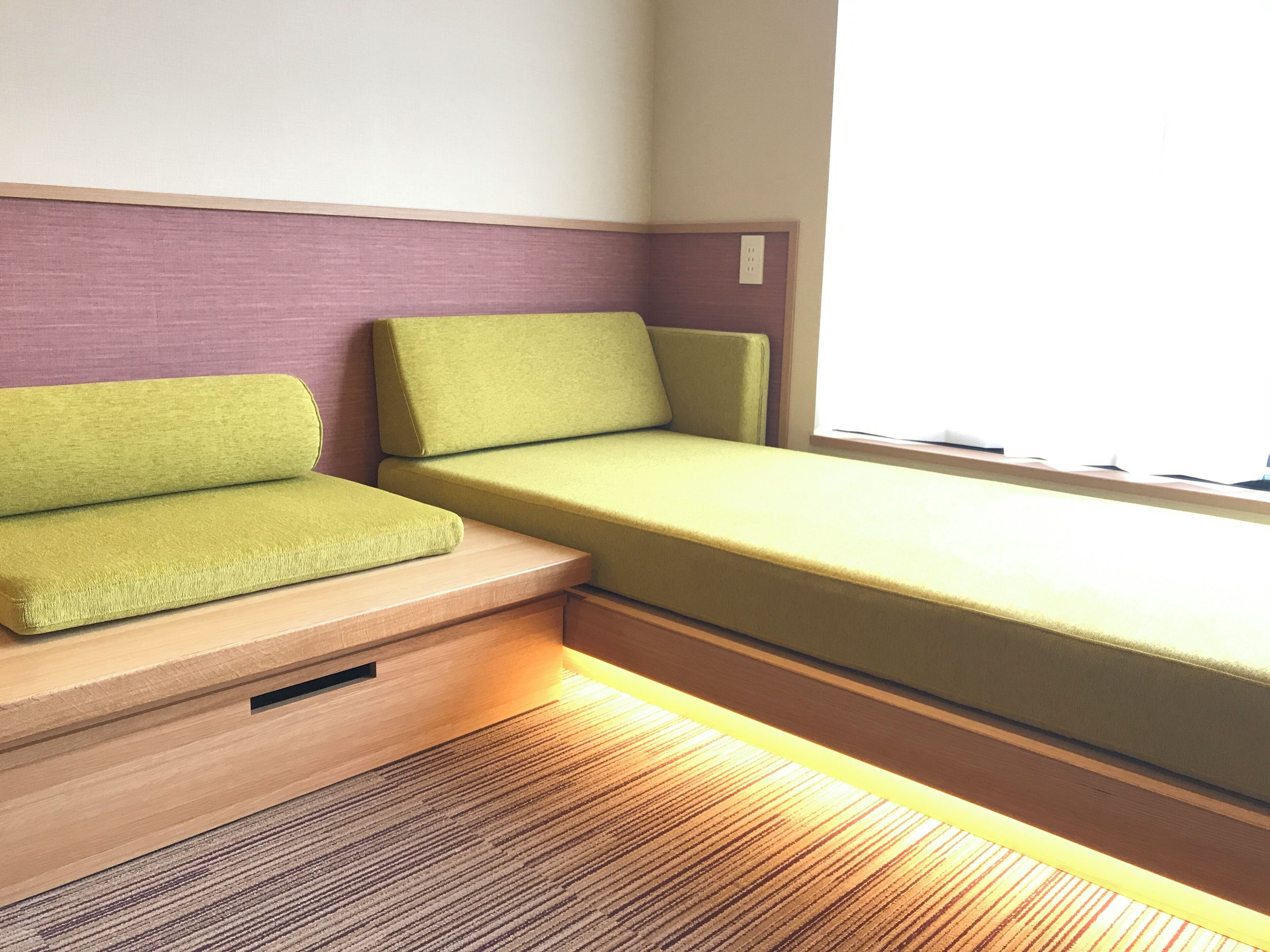 A small, compact room with a bed, a bench, and a window.