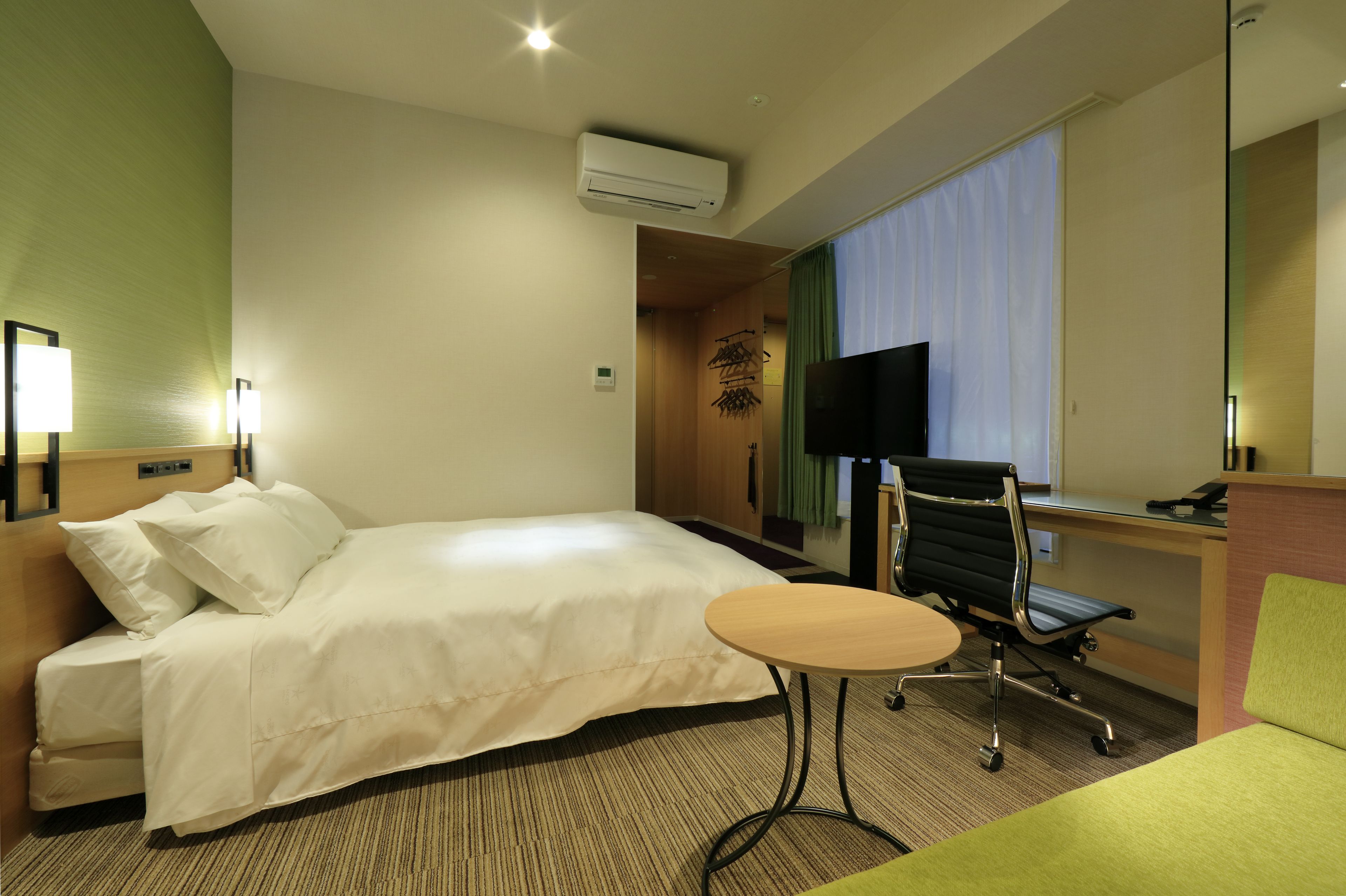 A hotel room with a bed, a desk, a chair, a small table, and a TV.