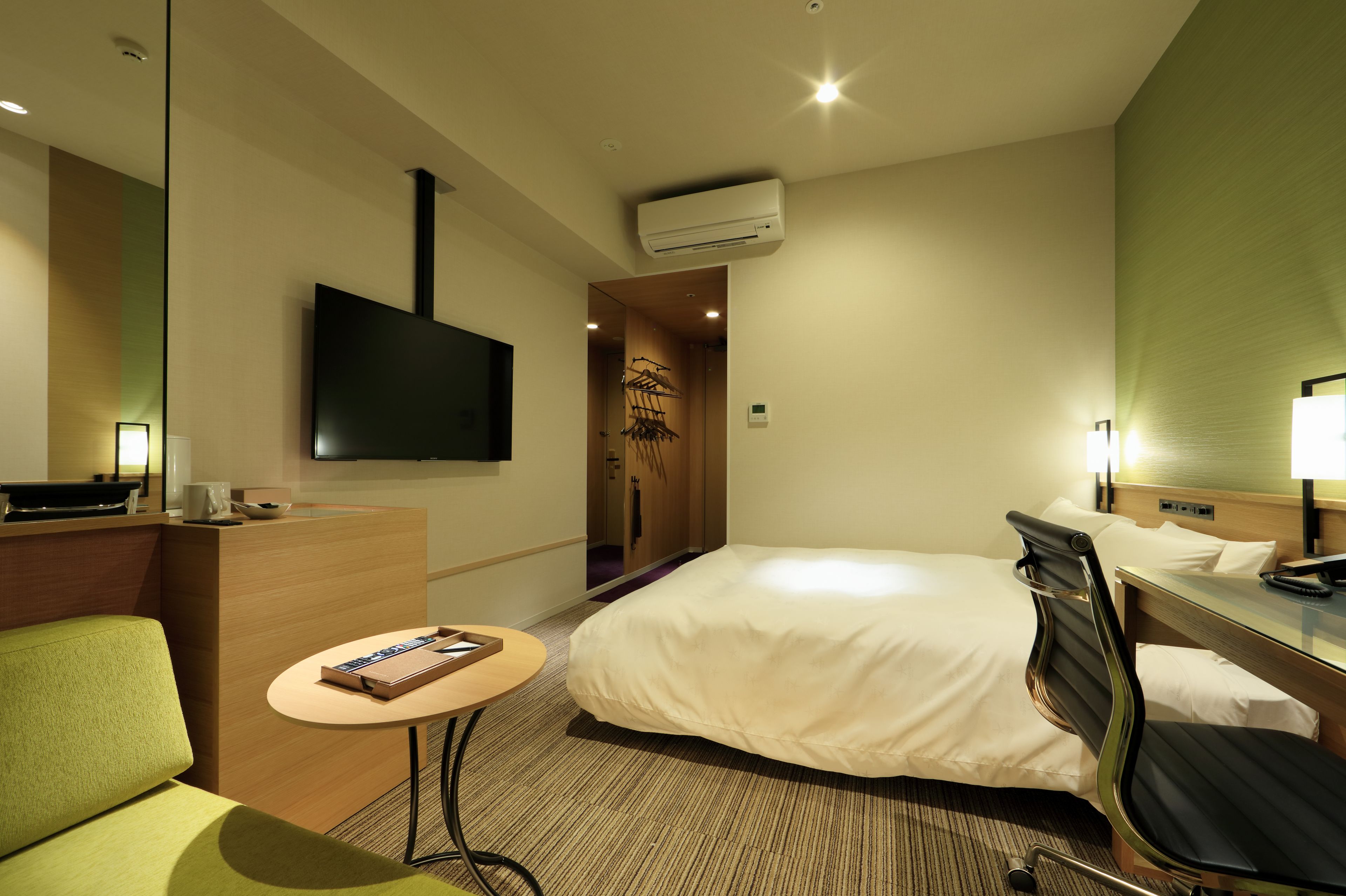 Une chambre d’hôtel équipée d’un lit, d’un bureau, d’une chaise, d’une petite table, d’un téléviseur et d’un appareil de climatisation.