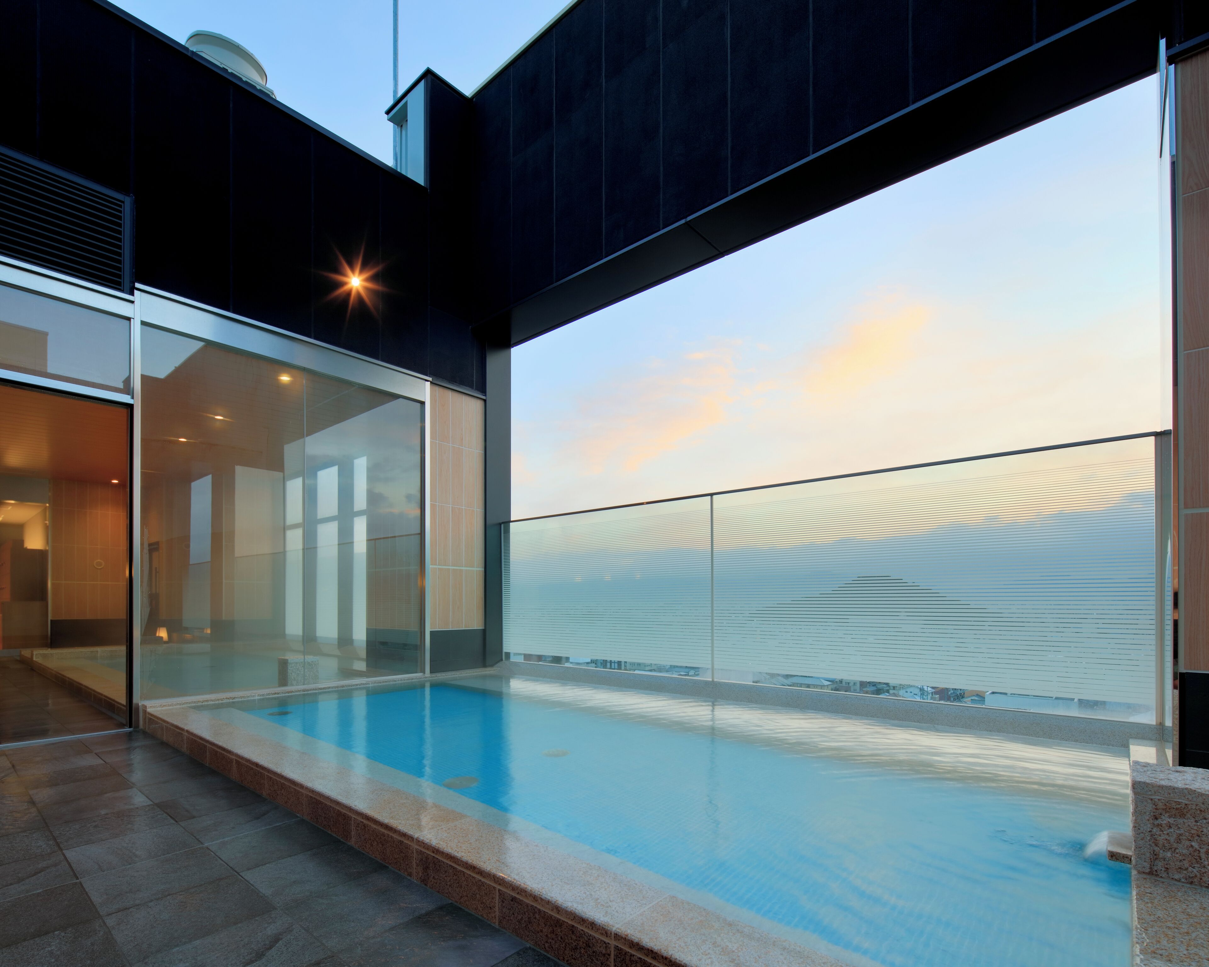Un edificio moderno con piscina infinita de cristal, cielo despejado y vistas al atardecer.