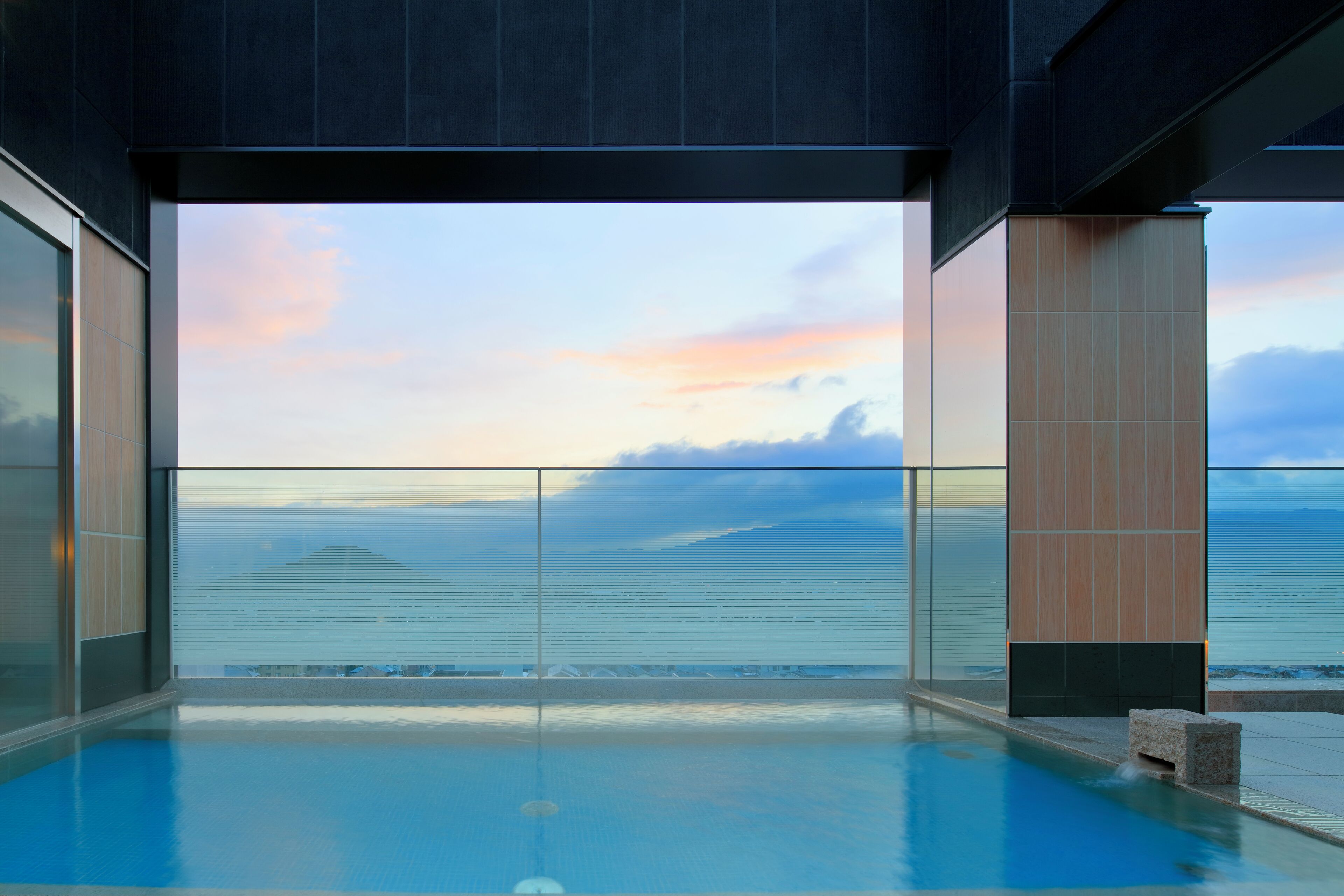 Una piscina infinita moderna con vistas claras al océano y un atardecer.