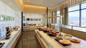 A buffet with various food items, a marble wall with a logo, and large windows offering a city view. - Candeo Hotels Nara Kashihara (Kashihara)