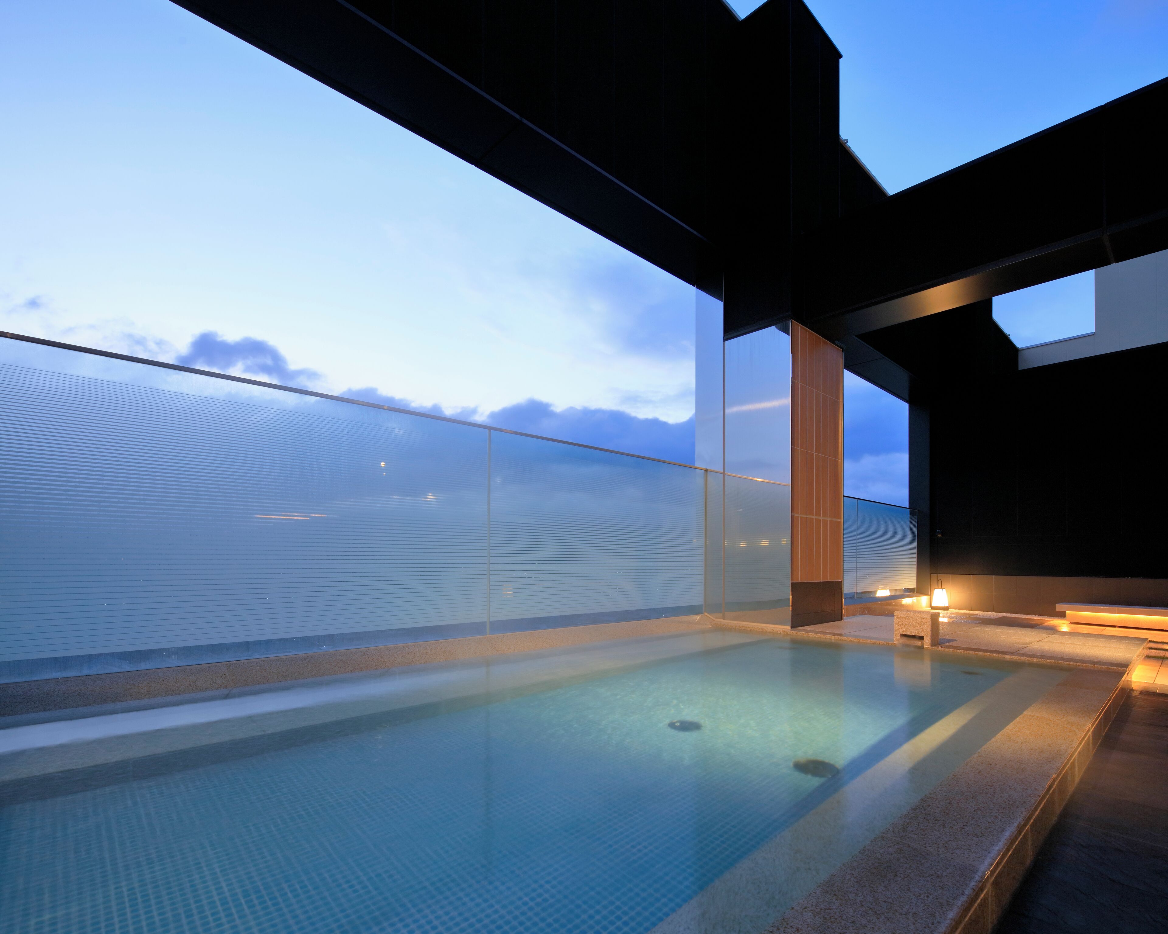 A modern outdoor pool with glass railings, a clear view of the sky, and a minimalist architectural design.