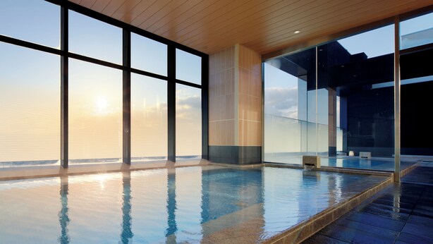 A large indoor swimming pool with clear glass walls, a tiled floor, and a wooden ceiling. - Candeo Hotels Nara Kashihara (Kashihara)