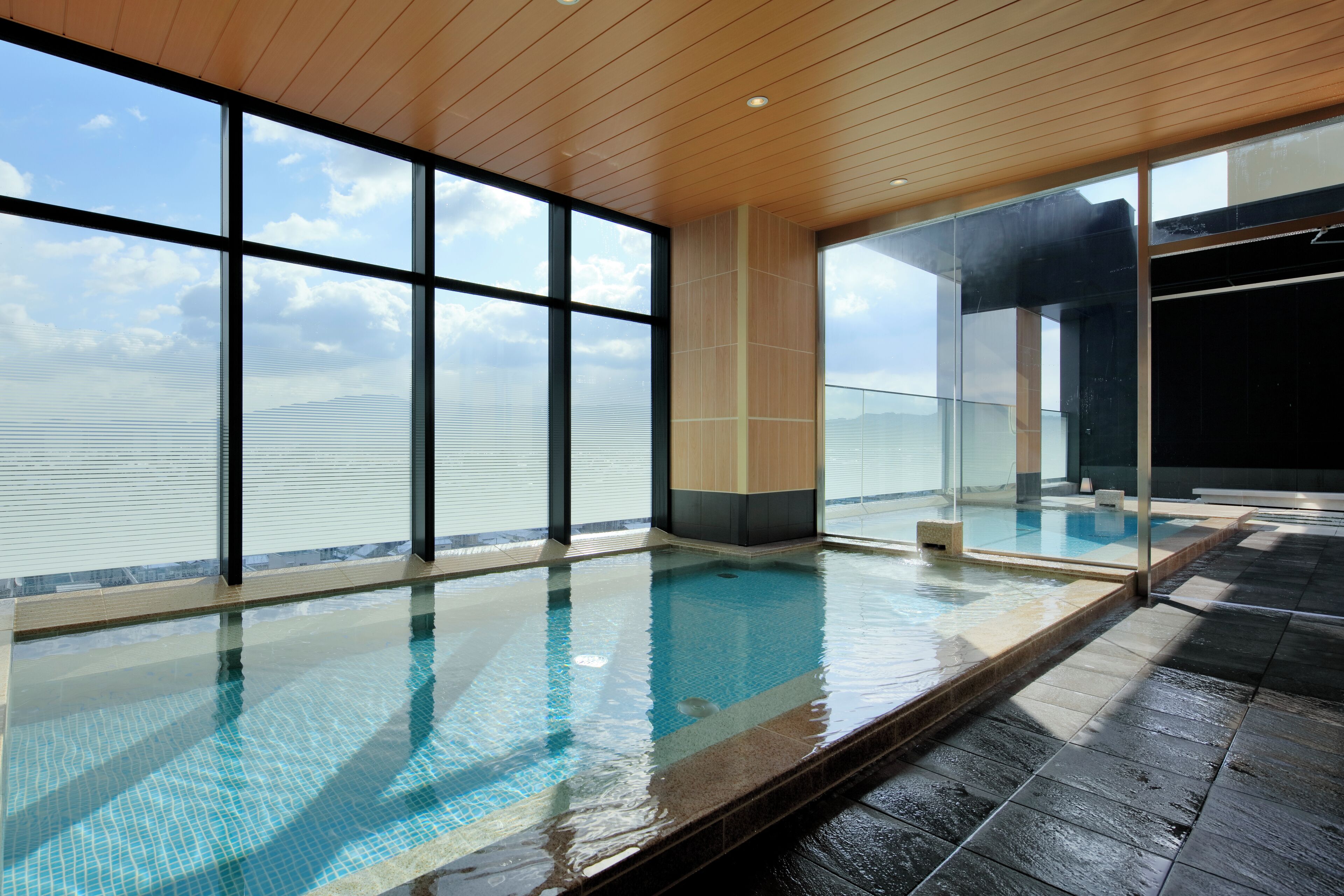 A large indoor swimming pool with clear glass walls, a wooden ceiling, and a view of the sky.